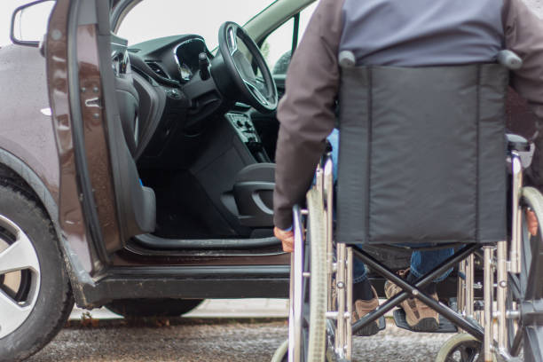 A man in a wheelchair trying to get into the driver's seat of a car stock photo