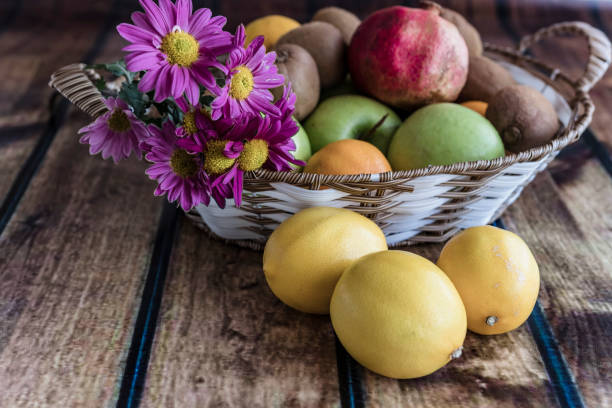 Close-up View of Delicious Fruit in the Bowl on Wooden Table in Home Interior Decorated with Pink Daisies Flowers.