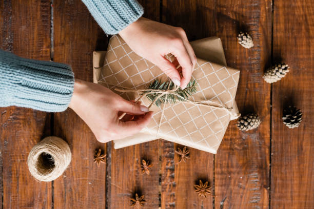 chica manos nudo de unión en la parte superior de la caja de regalo entre piñas y anís estrellado - heart shape christmas paper christmas gift fotografías e imágenes de stock