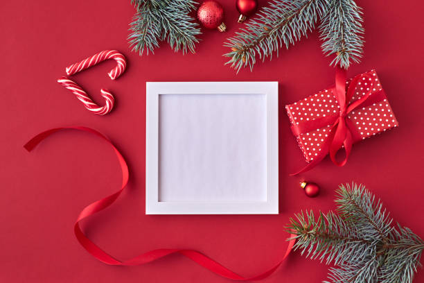 istock Mockup square white frame with red christmas balls, spruce branches and gift box on a red background 1185085530