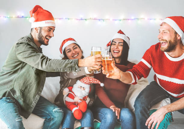 group of happy friends cheering with beer at christmas party - young people having fun drinking and enjoying together xmas holidays - friendship, drinks and youth celebrating lifestyle concept - life events laughing women latin american and hispanic ethnicity imagens e fotografias de stock
