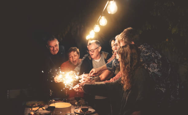 happy family having fun at dinner night party outdoor - group of people mixed ages celebrating together with fireworks sparklers outside - holidays culture and parenthood lifestyle concept - dining senior adult friendship mature adult imagens e fotografias de stock