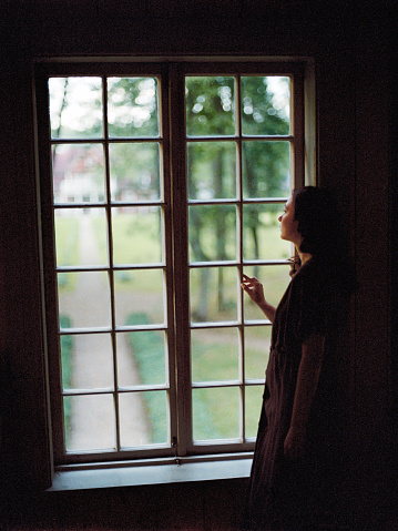 Young Caucasian woman standing near the window in old-fashioned house