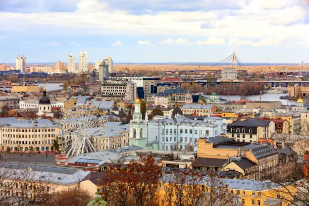 Photo of The landscape of the autumn city of Kyiv overlooking the old district of Podil with a Ferris wheel and a bell tower with a gilded dome, the Dnipro River and many bridges.