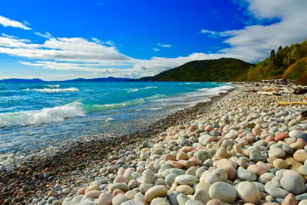 Beach cobble stones create a balancing contrast to the colours and texture of the cold waves, green boreal forest and blue skies of Lake Superior`s northern shore.