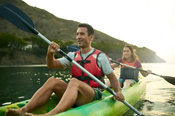 Close-up of active Spanish couple paddling tandem kayak off the Costa Brava in Mediterranean Sea at dawn.