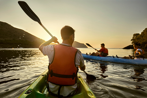 Rear view close-up of Spanish male kayaker in mid 40s paddling with friends off the Costa Brava at sunrise.