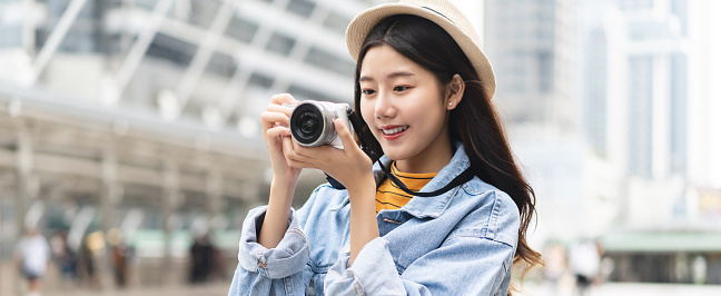 Young pretty Asian woman tourist solo traveling and taking pictures with camera in Bangkok city banner background