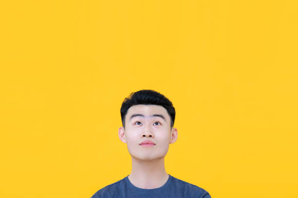 Thoughtful young Asian man looking up to copy space