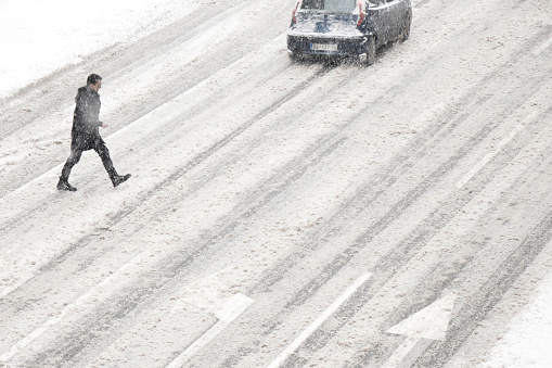 Belgrade, Serbia- January 26, 2019: One man crossing the street outside of crosswalk during the snowstorm and a driving car, high angle view