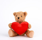cute brown teddy bear holding a big red heart on a white background