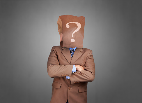 Portrait of businessman in disguise, wearing blank empty paper bag mask covering his face with question mark symbol on it, anonymous person concept