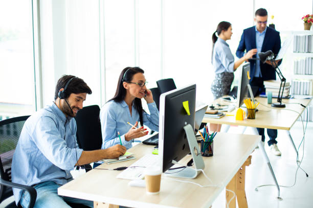 istock Attractive business people in headsets are smiling while working with computer in modern office 1185135509