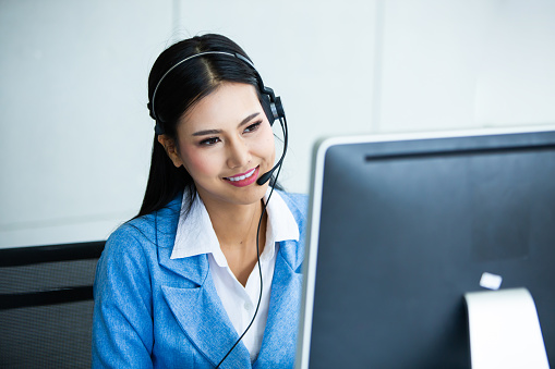 Atractiva mujer de negocios asiática en trajes y auriculares sonríen mientras trabaja con la computadora en la oficina. Asistente de servicio al cliente que trabaja en la oficina photo