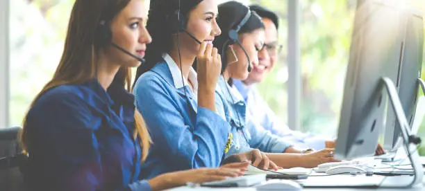 Photo of Attractive business woman and business man with headsets are smiling while working with computer in office