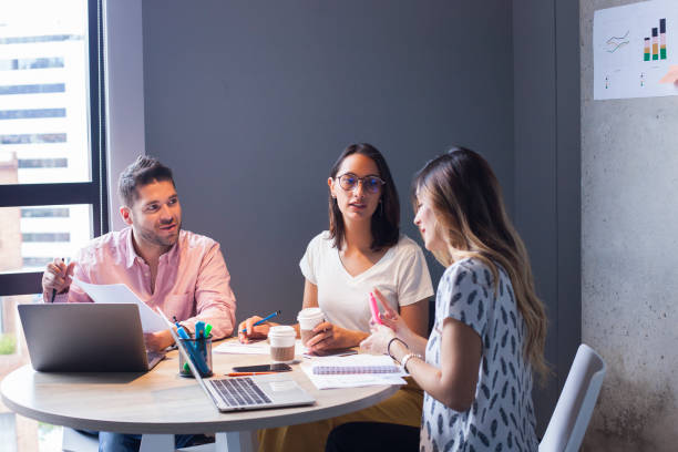 Coworkers discussing topics to improve the business Co-workers of ethnicity between the ages of 25-35 are in the office with their laptops discussing topics to improve the business latin script stock pictures, royalty-free photos & images