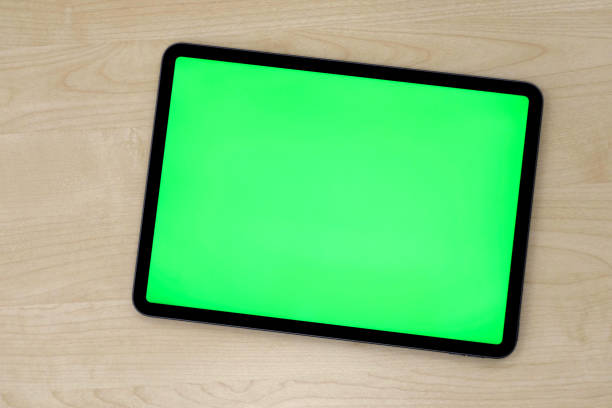 Top view of green screen tablet device on patterned wooden table