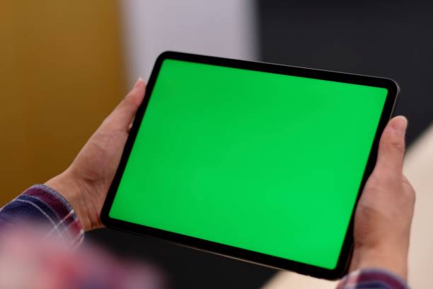 istock Over shoulder of one man holding green screen tablet pc in office. 1185151545
