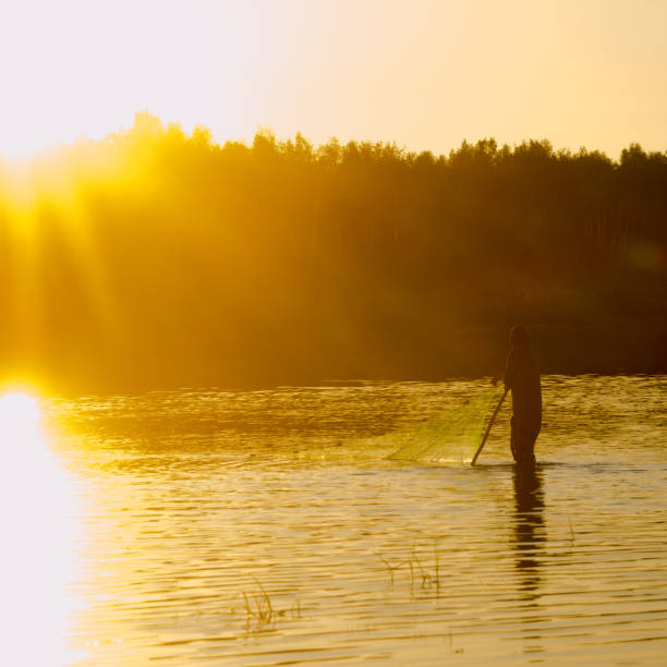 istock A lonely man, a Yakut fisherman in wading boots resting based on the dragnet network for wildlife in the river Vilyuy in the bright rays of the sun catching the local fish chugunok. 1185165234