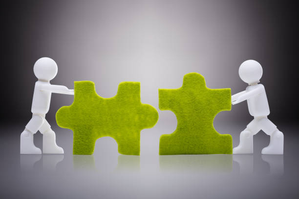 Two White Human Figures Joining The Green Jigsaw Pieces On Gray Background