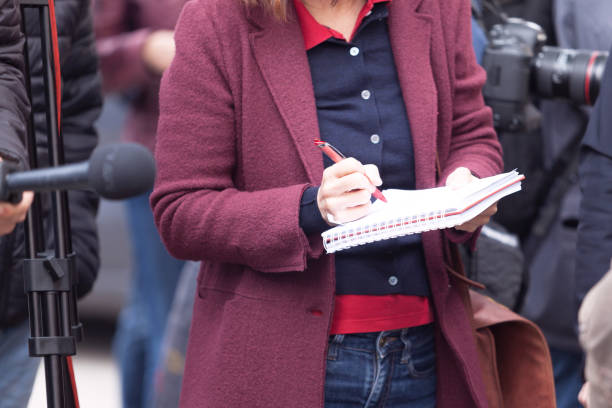 Female journalist at news conference or media event, writing notes, holding microphone Female reporter at press conference, writing notes, holding microphone release notes stock pictures, royalty-free photos & images