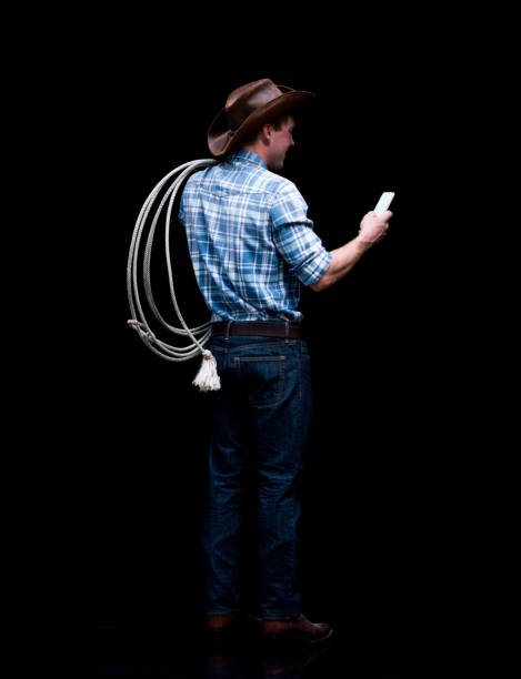 Full length / rear view / back / one man only / one person of 20-29 years old adult handsome people caucasian male / young men cowboy standing in front of black background / cool attitude and holding mobile phone / lasso / using smart phone / rope Full length / rear view / back / one man only / one person of 20-29 years old adult handsome people caucasian male / young men cowboy standing in front of black background wearing cowboy hat / hat / cowboy boot / button down shirt / shirt / jeans / pants / lumberjack shirt / plaid shirt / cool attitude and holding mobile phone / lasso / using smart phone / rope / text messaging / black color checkered cowboy boots stock pictures, royalty-free photos & images