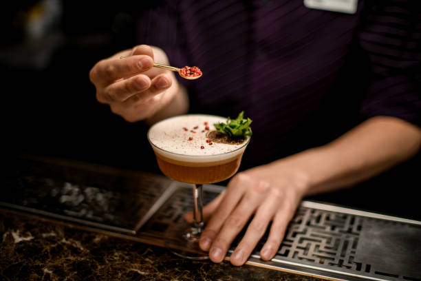 bartender añadiendo a un cóctel alcohólico decorando con una rama de menta verde y naranja seca un grano rojo de pimienta - drink on top of ice food fotografías e imágenes de stock