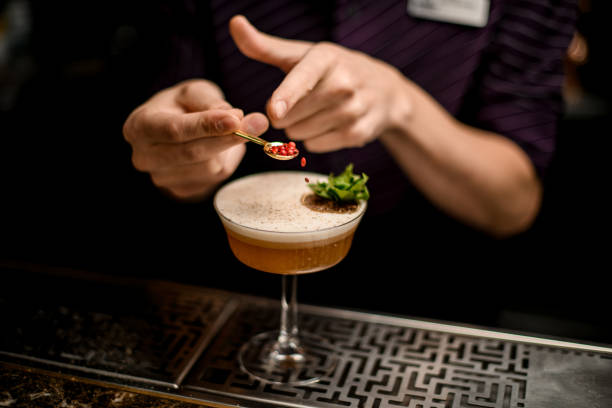 istock Male bartender adding to an alcoholic cocktail decorating with a green mint branch and dried orange a red peppercorns 1185184695