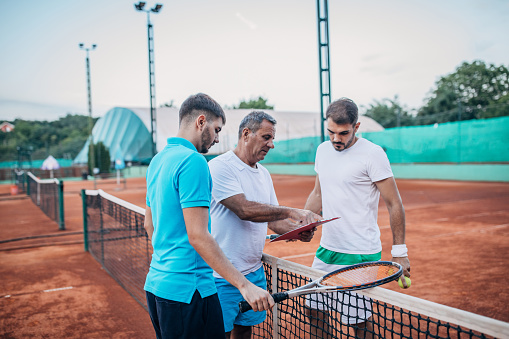 Coach teaching tennis lessons to men - outdoors sports concepts