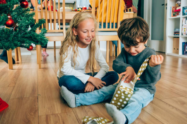 Christmas is time for presents Two kids sitting on the floor and opening christmas gifts near the Christmas tree. unwrapping stock pictures, royalty-free photos & images