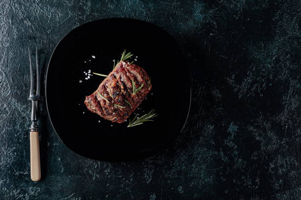 istock Grilled beef steak with rosemary and salt on a black plate. 1185193695