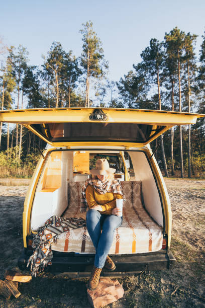 Young blonde Caucasian woman relaxing in her campervan at sunset stock photo