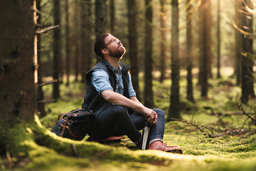 A man hiking through pine tree forests in Sweden. He is sitting down to drink some hot coffee.