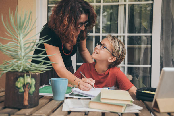 istock Young student doing homework at home with school books, newspaper and digital pad helped by his mother. Mum writing on the copybook teaching his son. Education, family lifestyle, homeschooling concept 1185202561