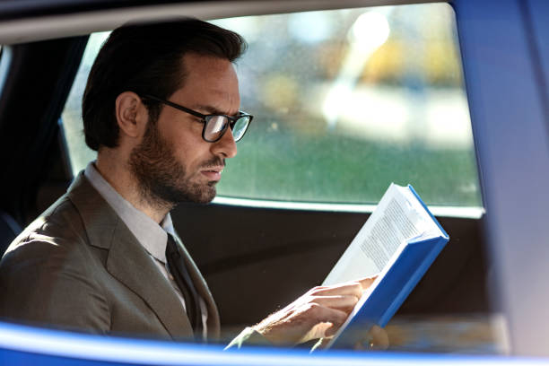 istock Young businessman sitting inside car and reading book 1185204733