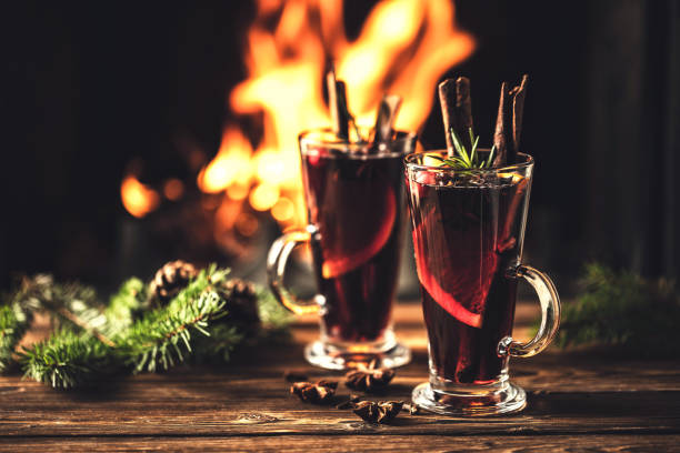 vino mullido con especias en vasos sobre una mesa de madera sobre el fondo de un fuego de chimenea. bebida de invierno tradicional para las vacaciones de navidad. - mulled wine punch cocktail christmas fotografías e imágenes de stock