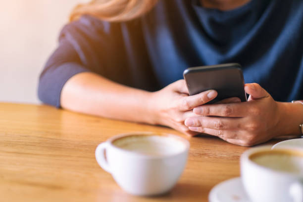 istock a woman holding  and using mobile phone with coffee cup on wooden table 1185204878