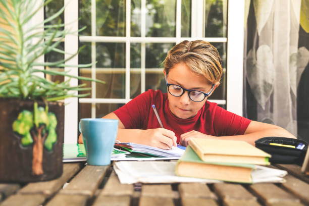 Young student doing homework at home sitting outdoor. Boy writing and studying with school books and newspaper. Kid doing a research and write on copybook. Education new technology lifestyle concept. joven estudiante haciendo la tarea en casa sentado al aire libre. niño escribiendo y estudiando con libros escolares y periódicos. un chico haciendo una investigación y escribe en un libro de texto. concepto de estilo de vida de nueva tecnología educat