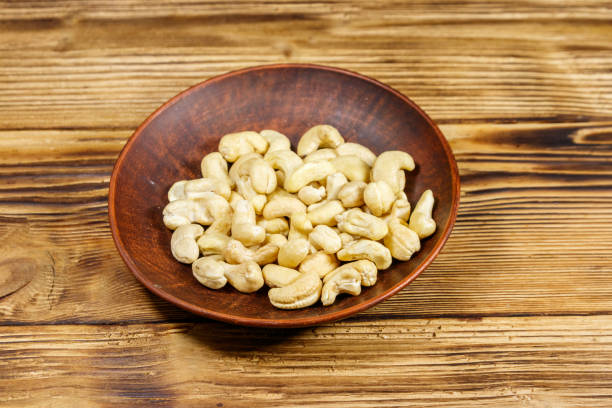istock Ceramic plate with raw cashew nuts on a wooden table 1185206966