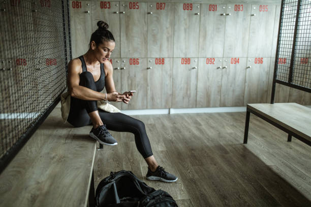 istock Sweaty athletic woman using cell phone in locker room. 1185207902