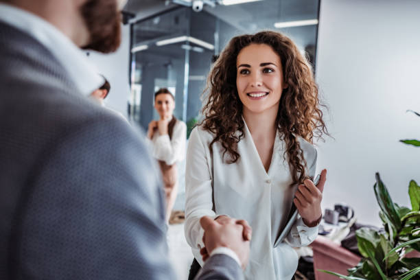 Greetings at work Waist up shot of beautiful young woman shaking hand to stylish businessman in office setting casual handshake stock pictures, royalty-free photos & images