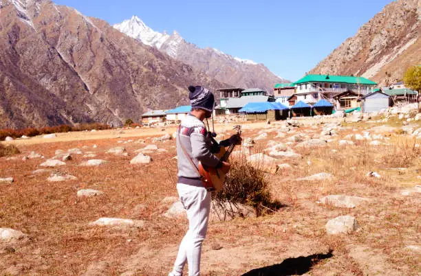 A solo traveler of Indian ethnicity and hobbyist  musician playing music with guitar on mountain valley. Alone in the silence of Himalayan mountain and sound of guitar strings. Summer music Inspiring environment in outdoors. Sangla Valley, Himachal Pradesh, India, South Asia.