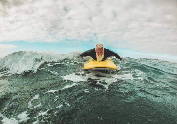 istock Senior man doing surf with longboard riding a wave - Happy old guy having fun doing extreme sport - Joyful elderly concept - Focus on his face 1185212409