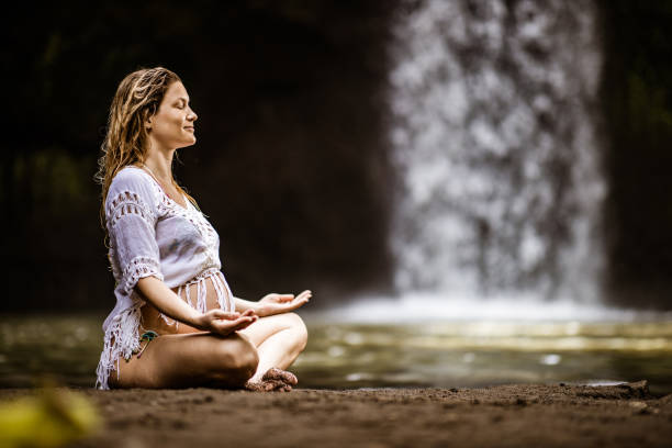una mujer embarazada sonriente meditando en posición de loto en la selva tropical. - waterfall zen like women meditating fotografías e imágenes de stock