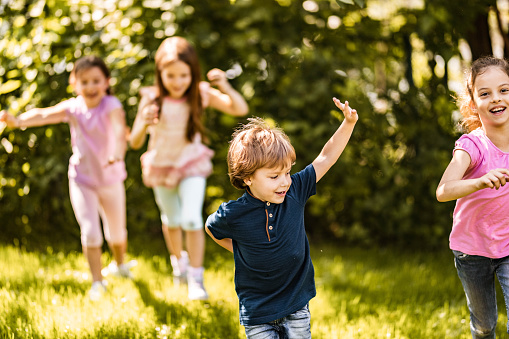 Group of happy kids having fun while running in springtime at the park.