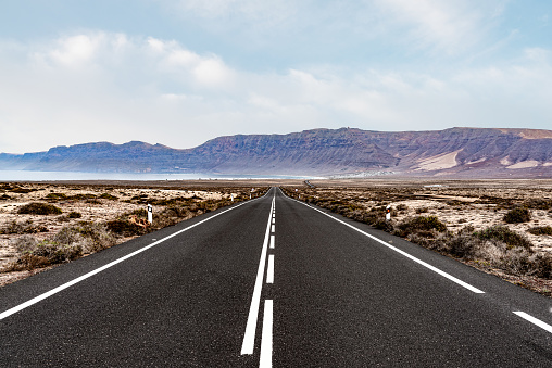long straight empty asphalt road through arid landscape against ocean and mountain range on Lanzarote, Canary Islands