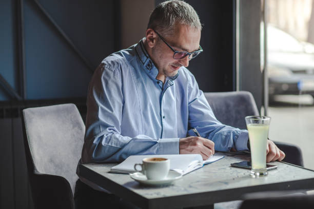 istock Smiling businessman writing in a notebook at cafe. 1185218646