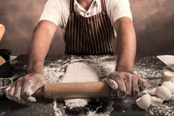 istock Man preparing buns at table in bakery, Man sprinkling flour over fresh dough on kitchen table 1185218691