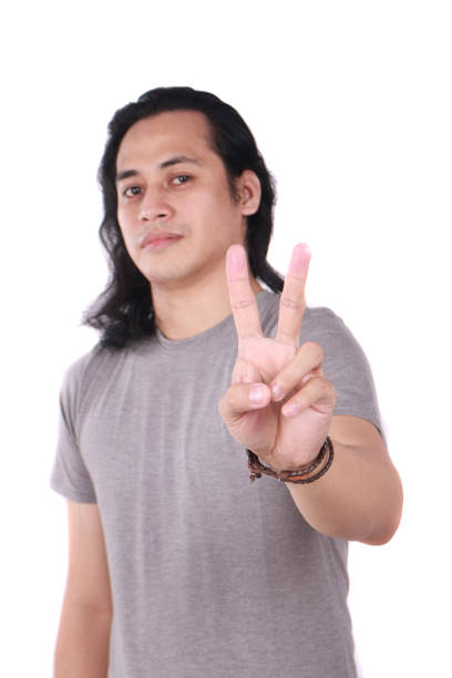 Portrait of good looking long haired young Asian man shows number two or peace sign gesture with his finger isolated on white