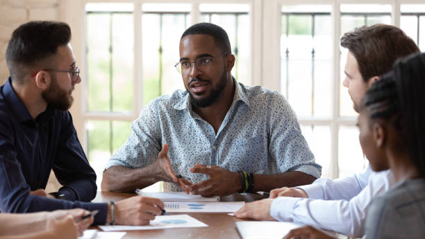 Concentrated african amrican male manager talking to diverse colleagues. Concentrated african amrican male manager talking to diverse colleagues at meeting in office. Serious mixed race professional discussing project strategy, explaining working issues to employees. serious talk stock pictures, royalty-free photos & images